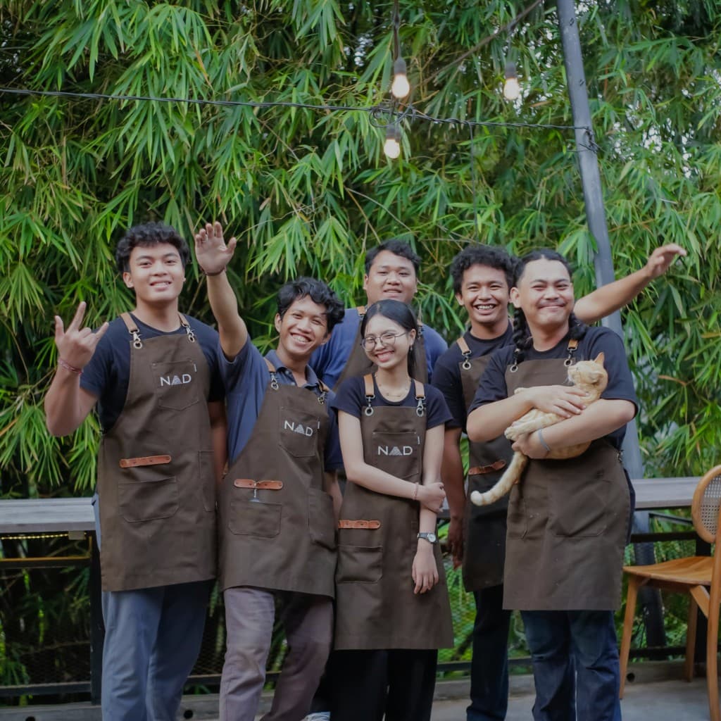 Restaurant team wearing aprons in front of bamboo foliage